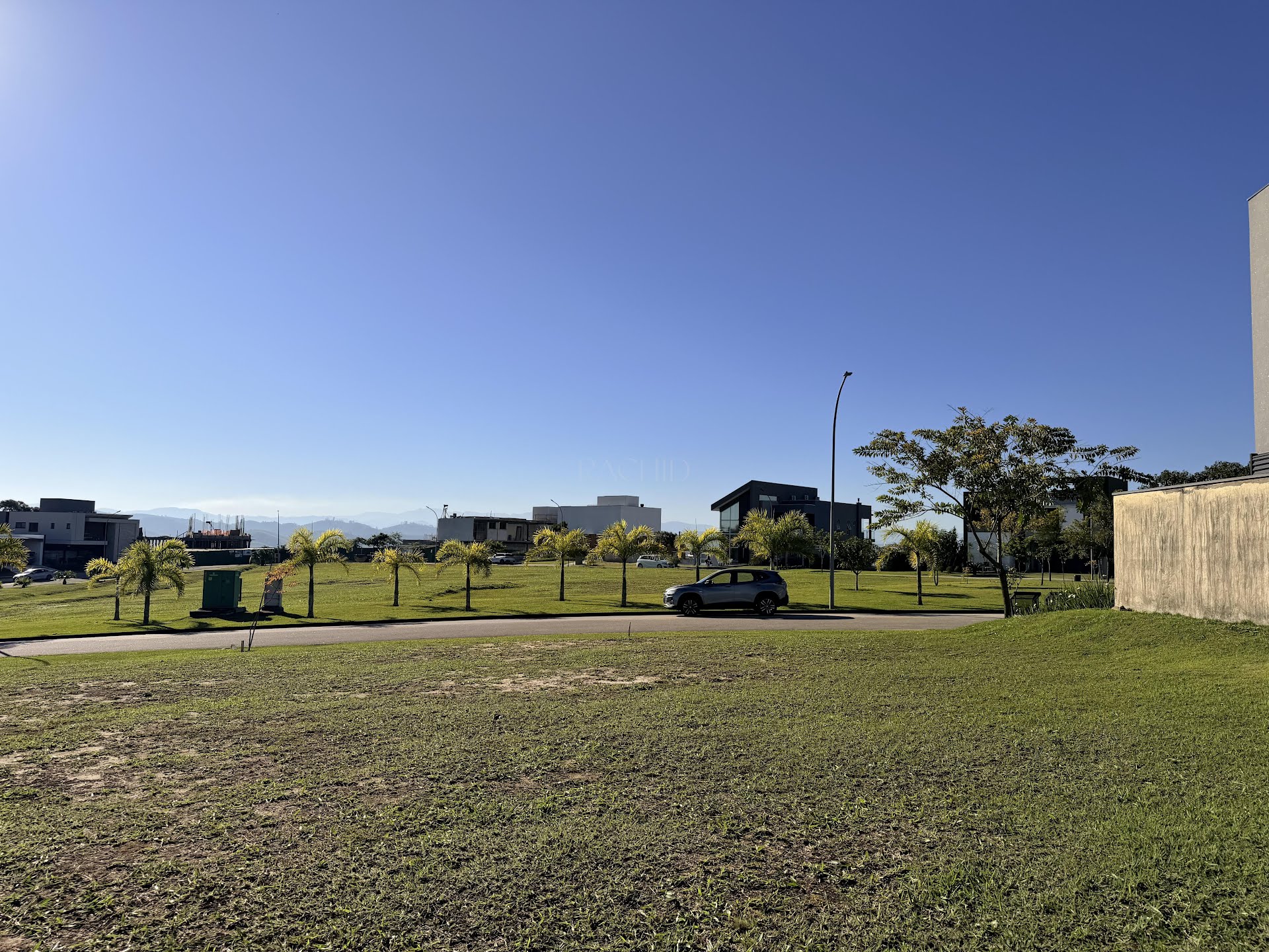 Rua arborizada do condomínio, com palmeiras e vista para a serra